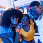 African woman singing karaoke with friends at home celebrating a night party