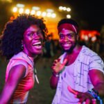 Young man and woman dancing and having fun together at a music festival, illuminated by colorful stage lights, creating a vibrant and energetic atmosphere