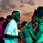 Happy young African couple dancing against their friends at rooftop party